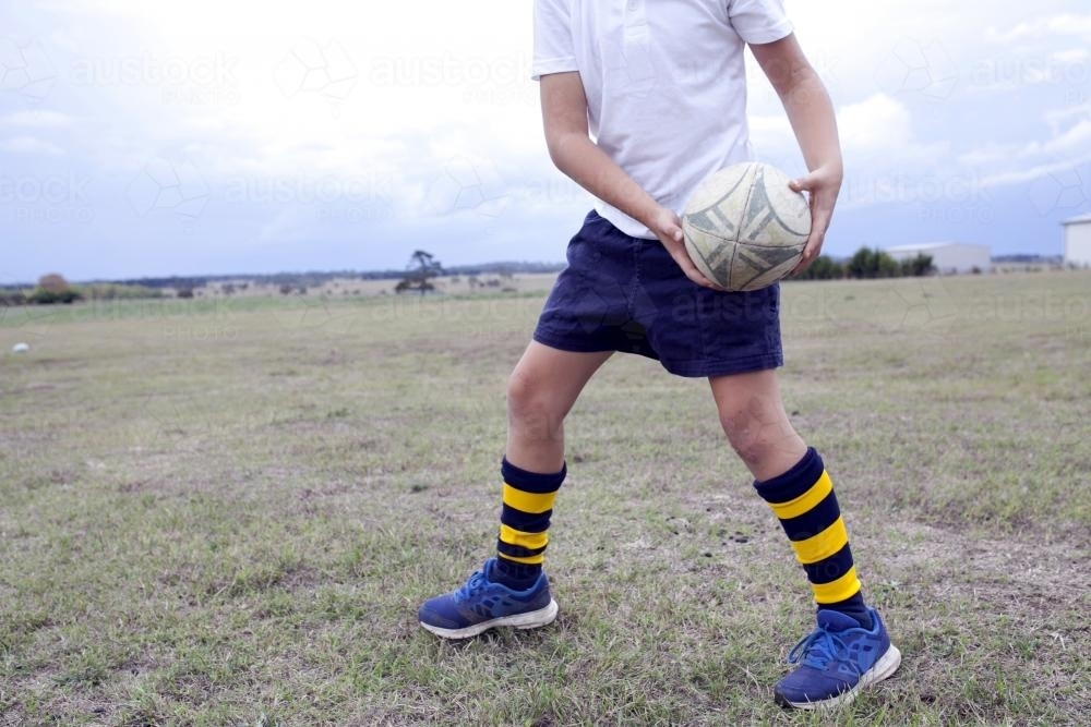 Detail of young boy passing a rugby ball in a paddock - Australian Stock Image