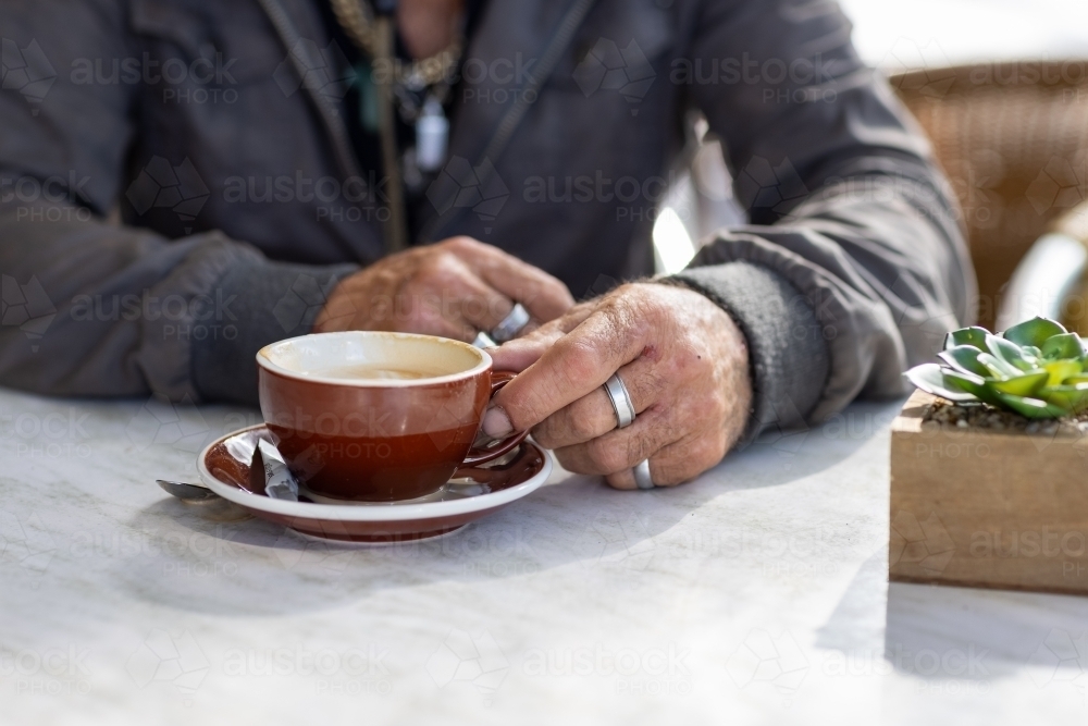 detail off unkempt man sitting at table with coffee and potplant - Australian Stock Image