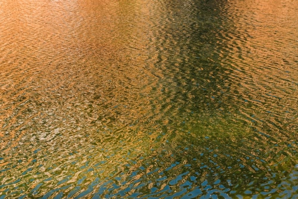 Detail shot of water with ripples and green and orange tones - Australian Stock Image