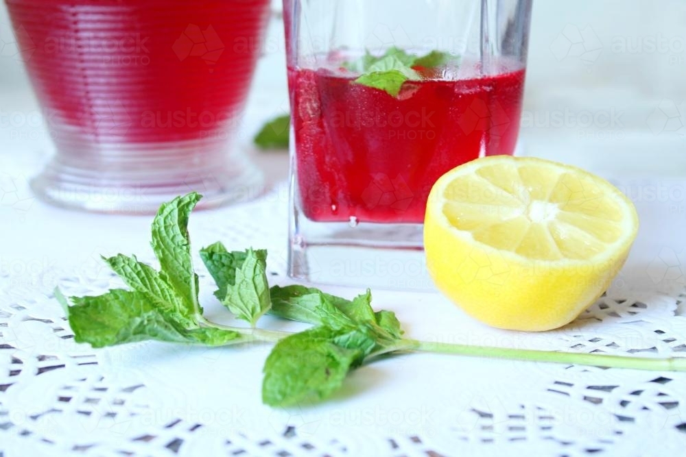 Detail view of refreshing red drink on table with lemon and mint - Australian Stock Image