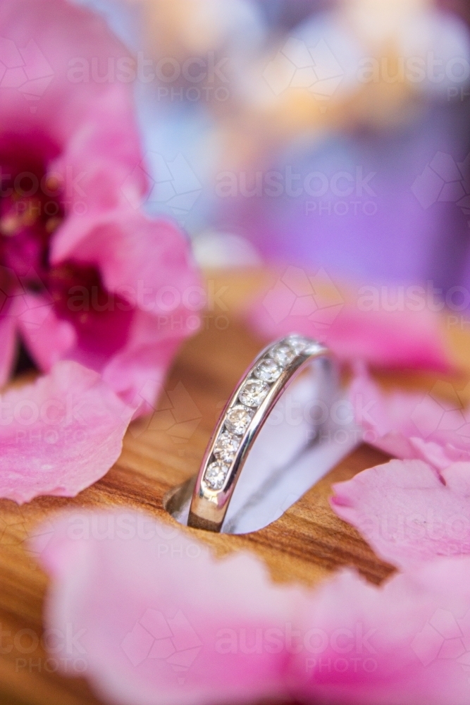 Diamond engagement ring in wooden box with flower petals around it - Australian Stock Image