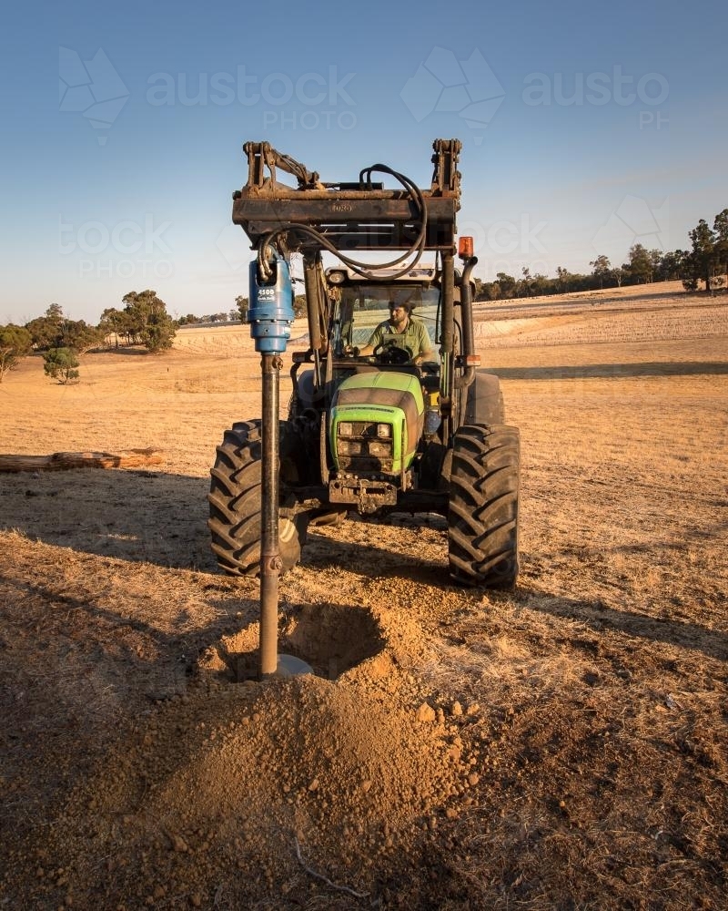Digging a hole with hydraulic posthole digger on tractor - Australian Stock Image