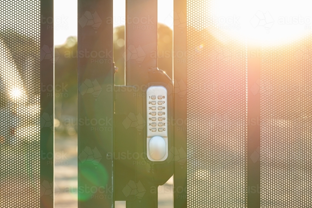 Digital smart lock on gate of fence around worksite with sun flare haze - Australian Stock Image