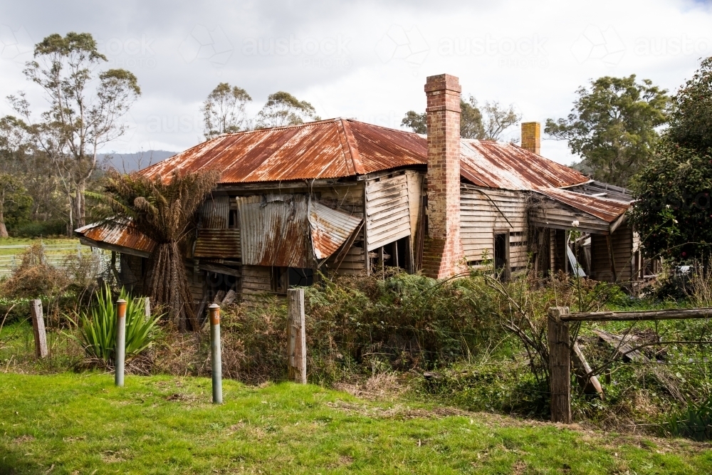 Dilapidated abandoned house surrounded by shrubs and trees - Australian Stock Image