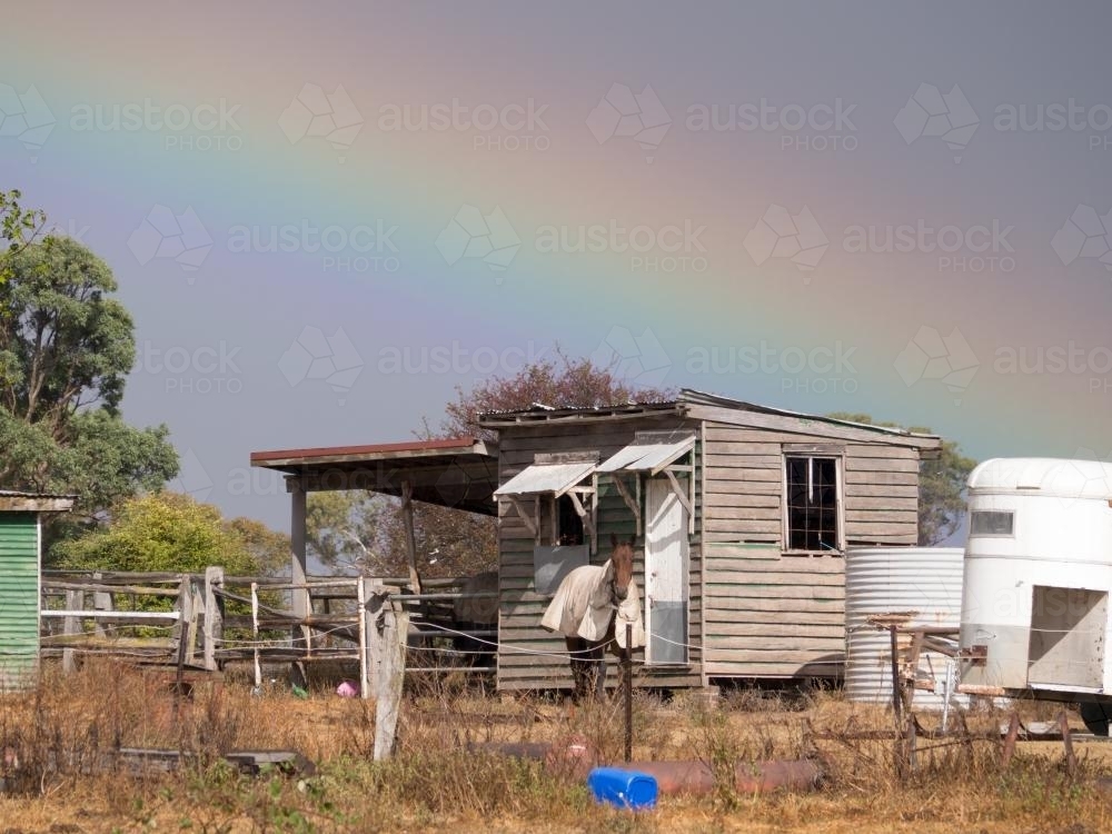 Dilapidated building with horses, rainbow and stormy sky - Australian Stock Image