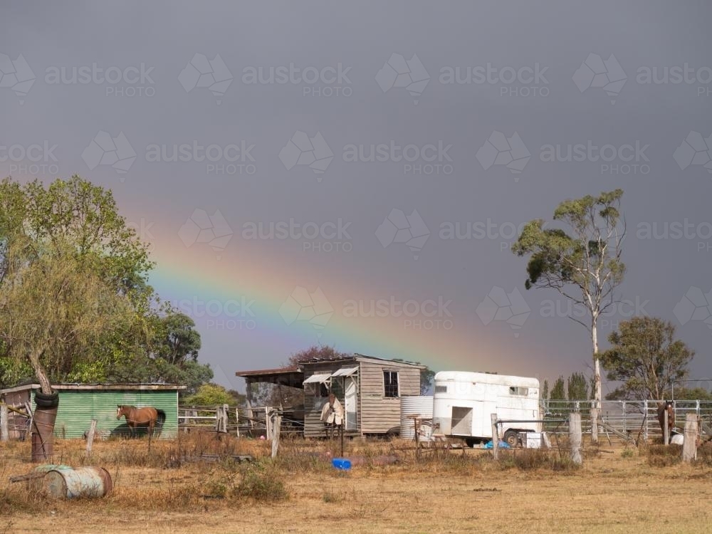 Dilapidated building with horses, rainbow and stormy sky - Australian Stock Image