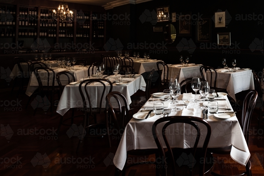 dim mood lighting in a restaurant with linen tablecloths and dinnerware laid out - Australian Stock Image