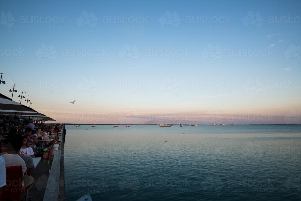 Diners at a wharf overlooking the harbour in the late afternoon light - Australian Stock Image