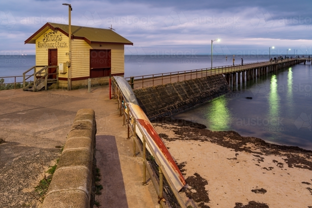 Dinghies leaning against a breakwater under a wooden kiosk at twilight - Australian Stock Image