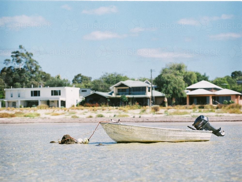 Dinghy moored in water with houses in background - Australian Stock Image