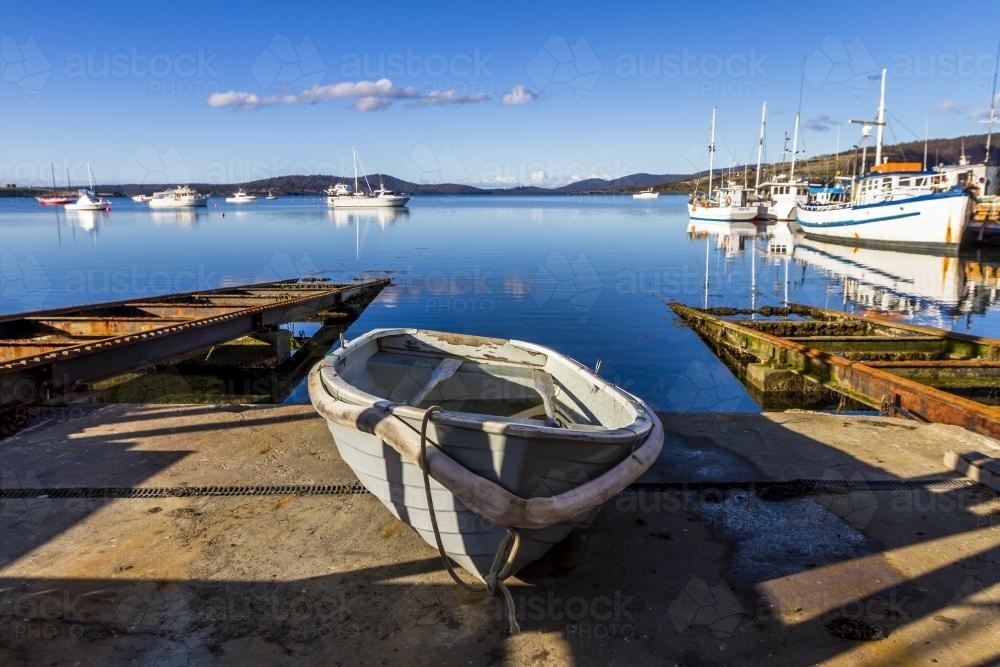 Dingy sitting on a slipway with other boats on the water - Australian Stock Image