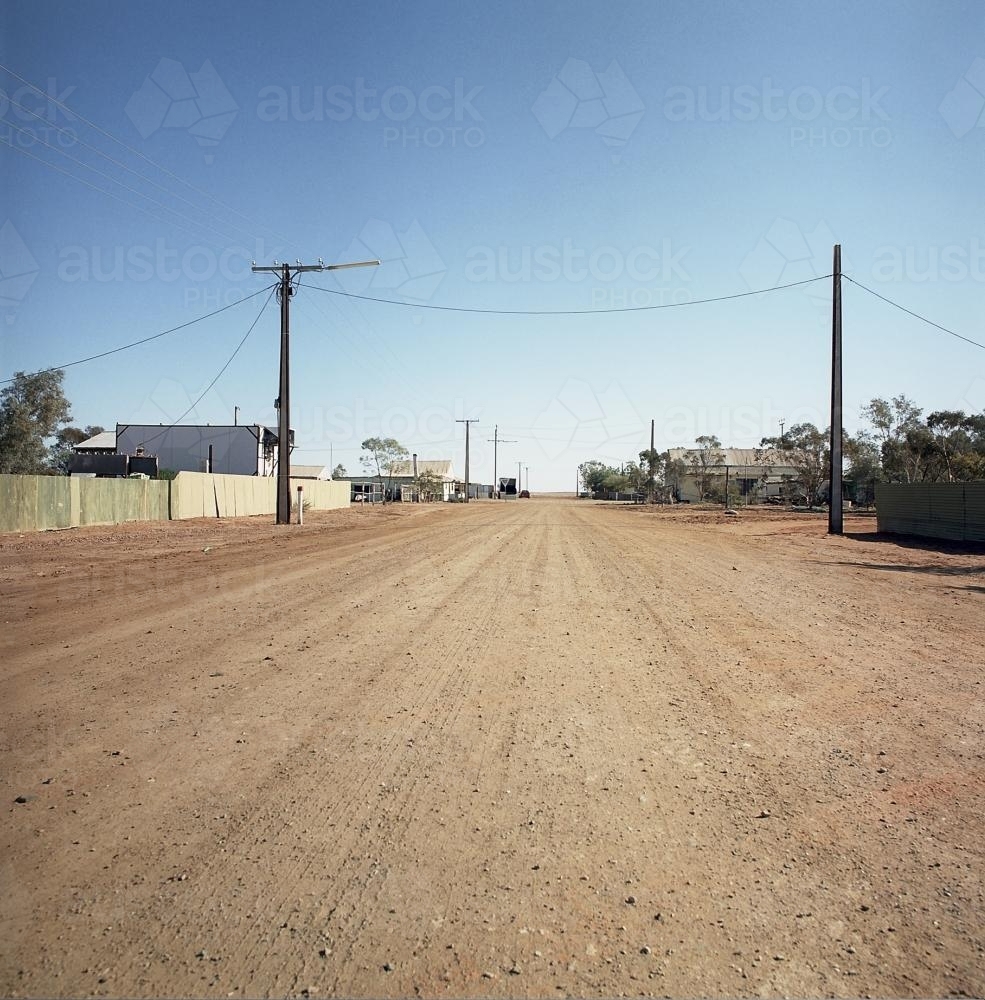 Dirt road in remote town with houses and power lines - Australian Stock Image
