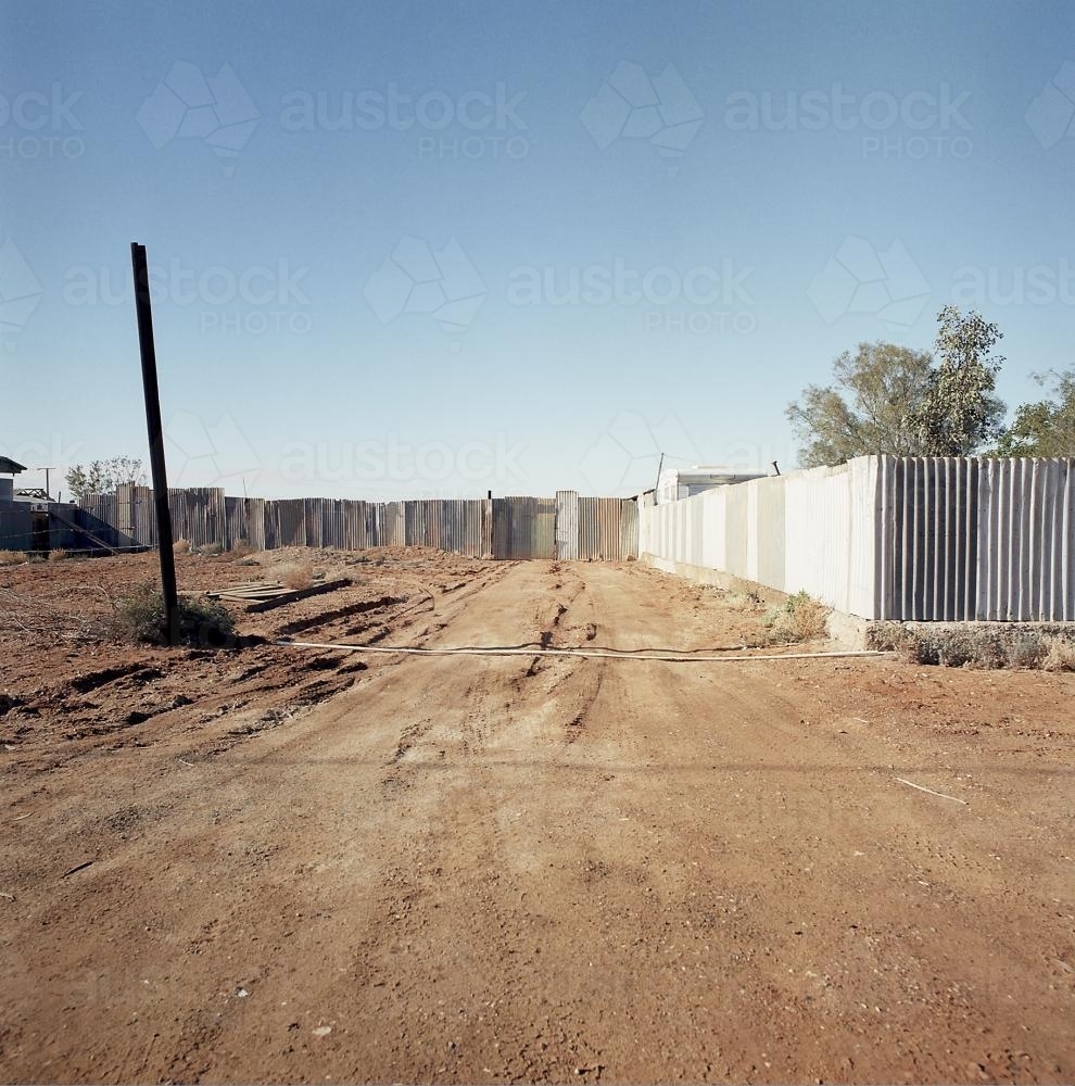 Dirt road in remote town with metal fence - Australian Stock Image