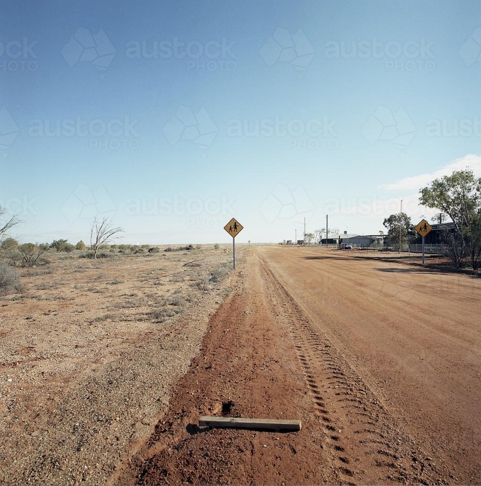 Dirt road in remote town with people crossing sign - Australian Stock Image