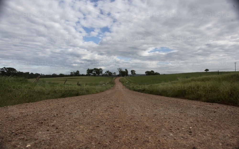 Dirt road leading into horizon, grass on both sides - Australian Stock Image