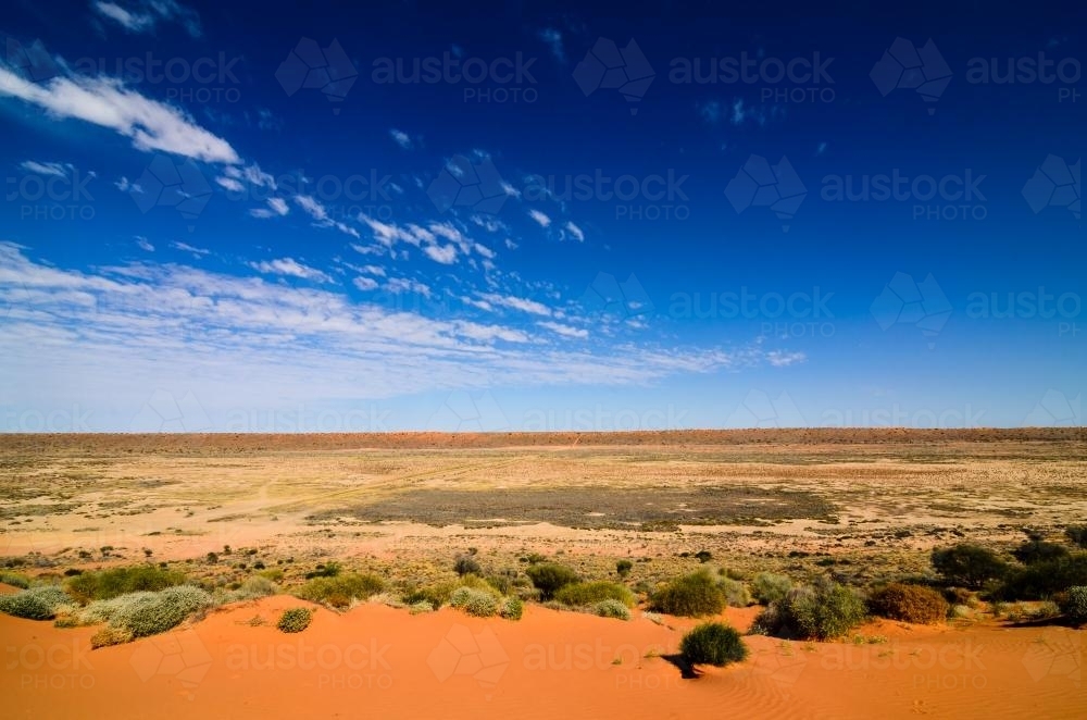 Dirt road leading off into the desert with dunes in the distance and dark blue sky - Australian Stock Image