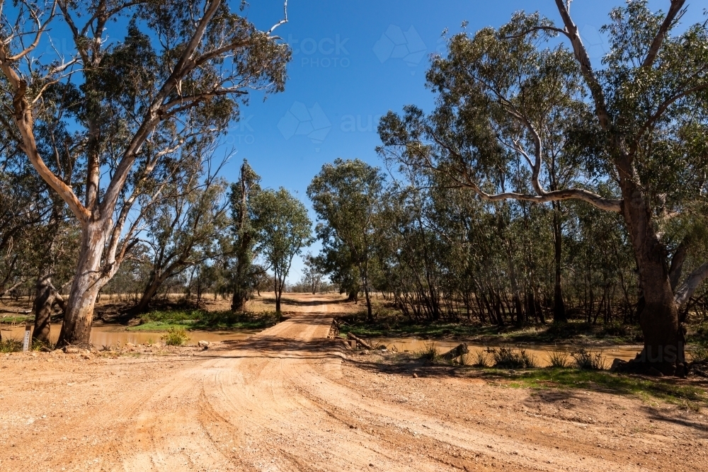 Dirt road leading to a creek crossing with trees and shadows. - Australian Stock Image