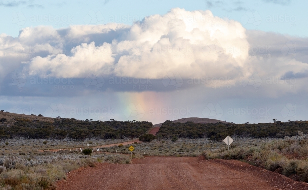 dirt road with storm clouds and rainbow on horizon - Australian Stock Image