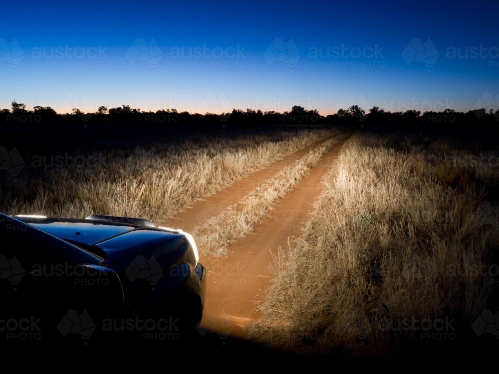 Dirt track through grassland lit by headlights - Australian Stock Image