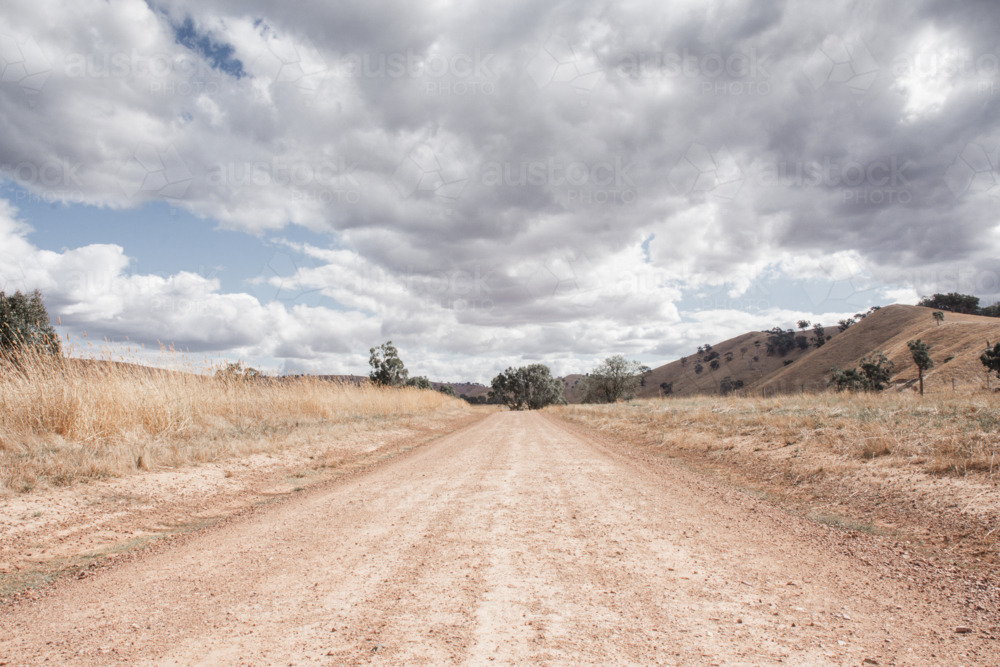 Dirt track with dry, summer grasses and cloudy sky - Australian Stock Image