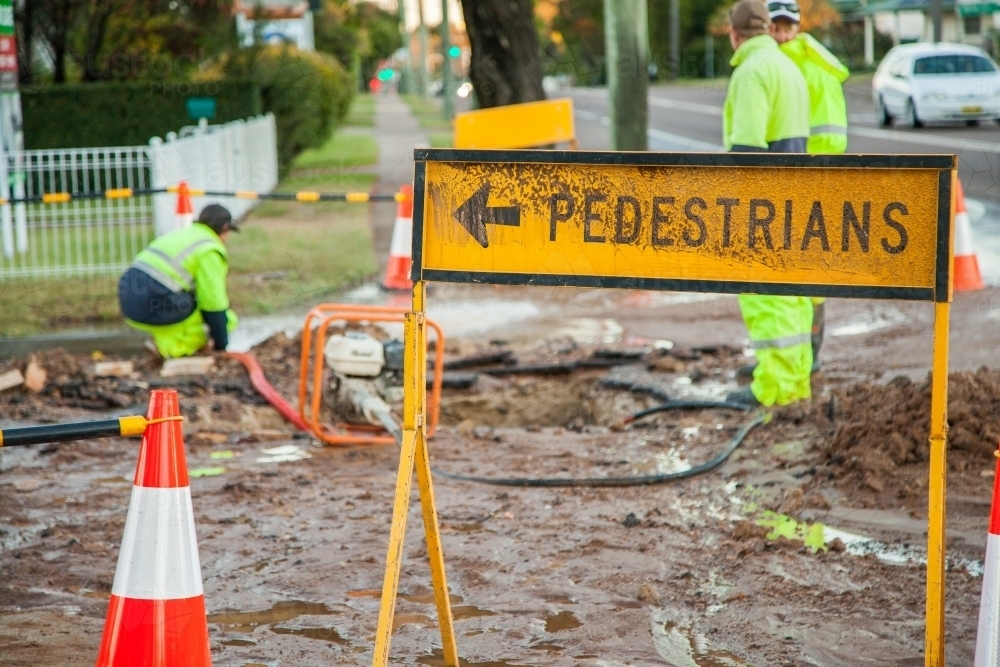Dirty pedestrians this way sign and muddy road from broken water main - Australian Stock Image
