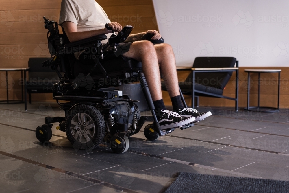 disabled man in motorised wheelchair, in foyer of apartment building - Australian Stock Image