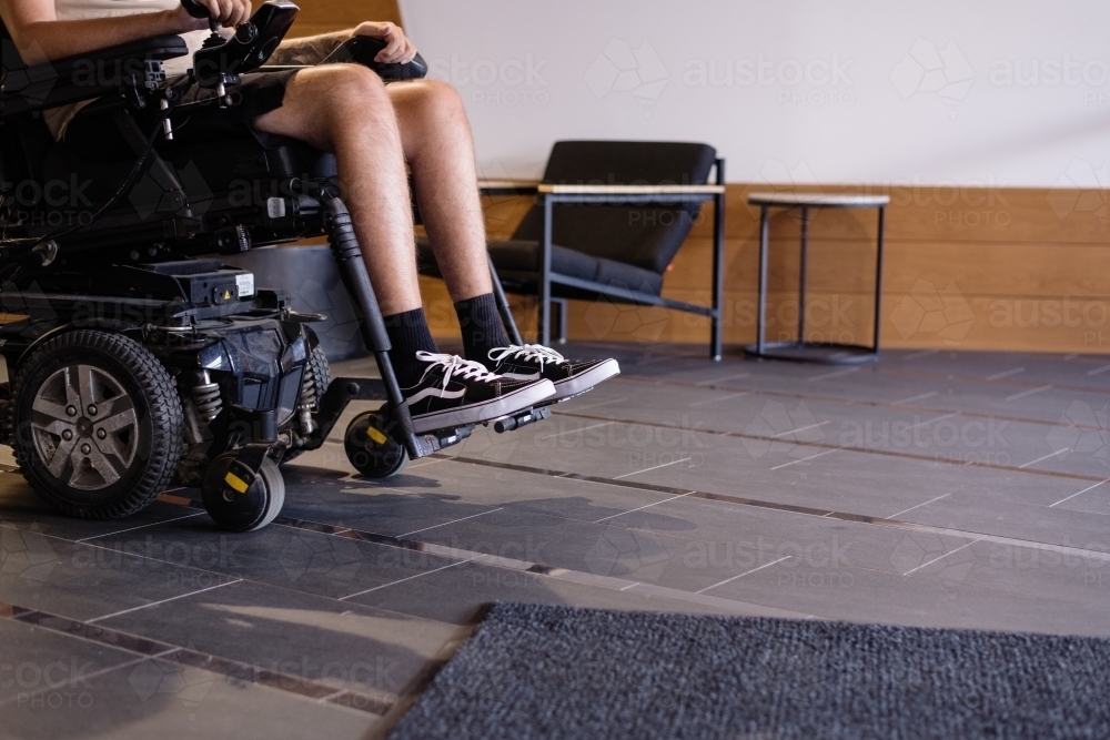 disabled man in motorised wheelchair, in foyer of apartment building - Australian Stock Image