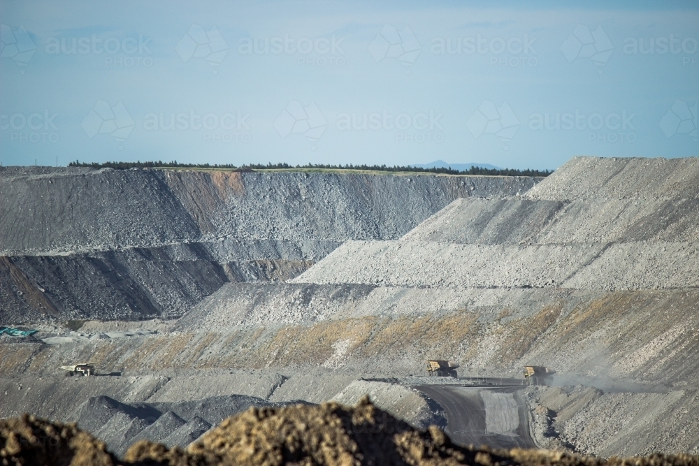 Distant dump trucks carting coal in grey hills of open cut mine - Australian Stock Image