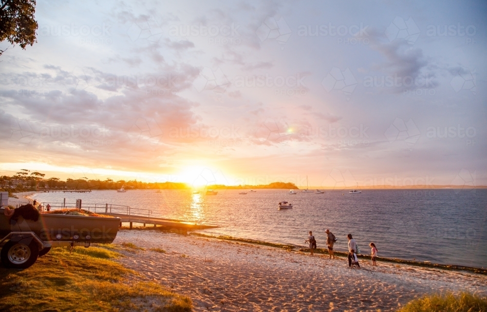 Distant family walking on a beach at sunset - Australian Stock Image