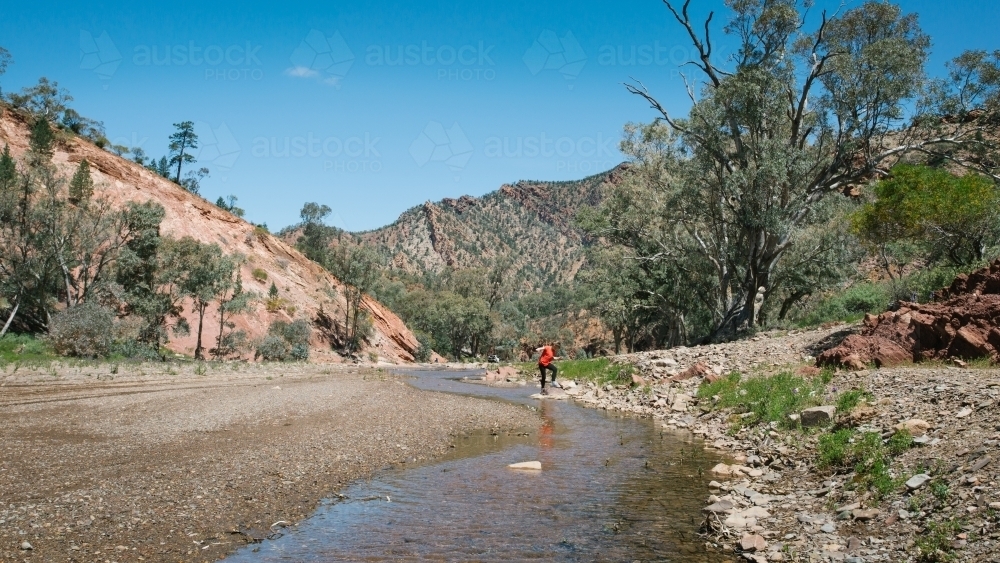 Distant figure standing in a creek in a remote rocky landscape - Australian Stock Image