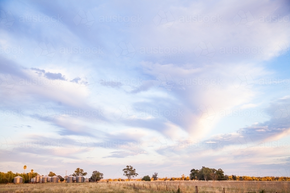 Distant grain silos in paddock landscape on a farm at dawn - Australian Stock Image