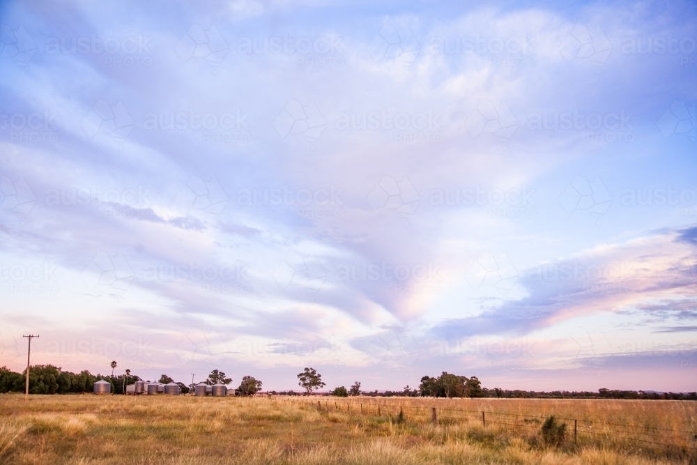 Distant grain silos in paddock landscape on a farm at dawn - Australian Stock Image