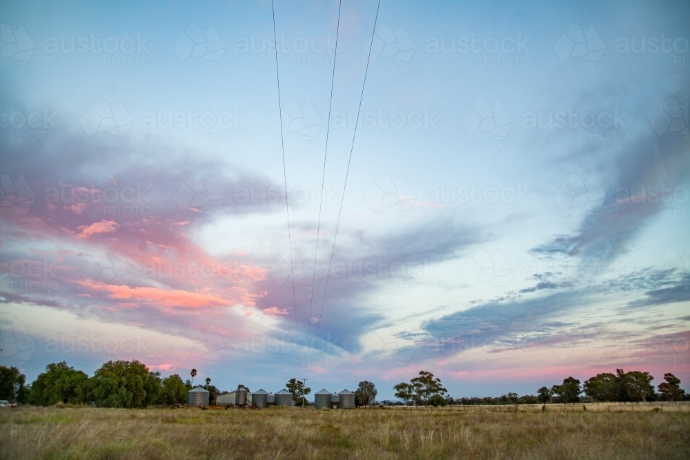 Distant grain silos in paddock landscape on a farm at dawn - Australian Stock Image