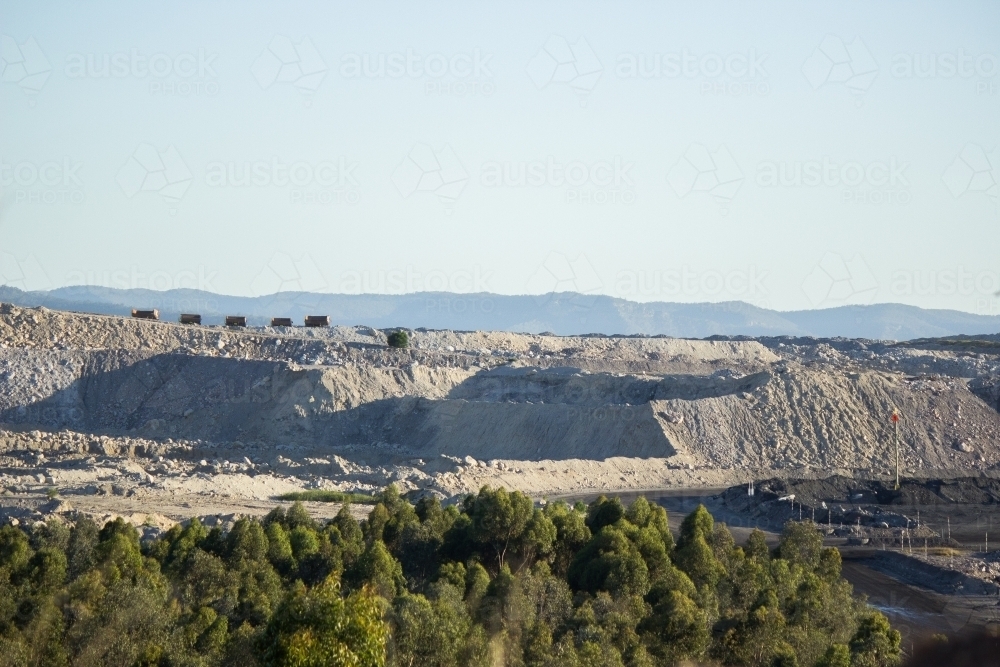 Distant hills of grey mining overburden and dump trucks - Australian Stock Image