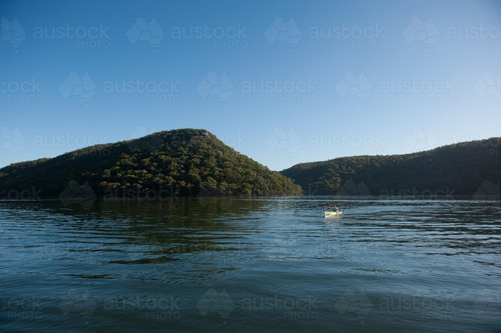 Distant man kayaking on lake with mountain view - Australian Stock Image