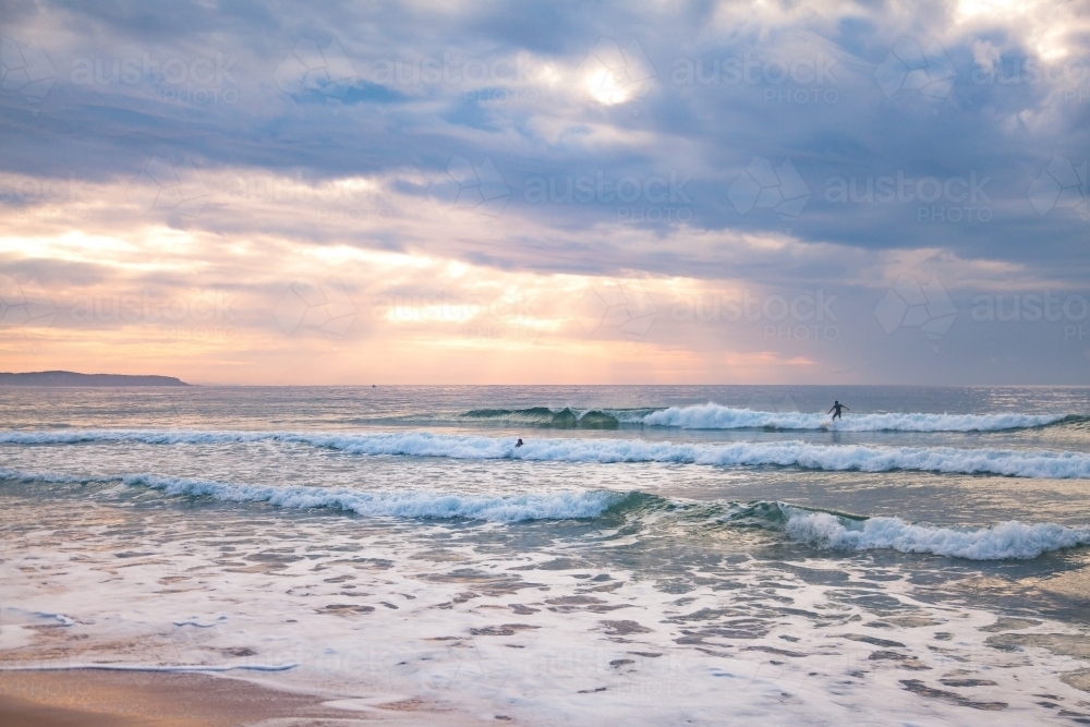 Distant person surfing on a small wave at sunrise - Australian Stock Image