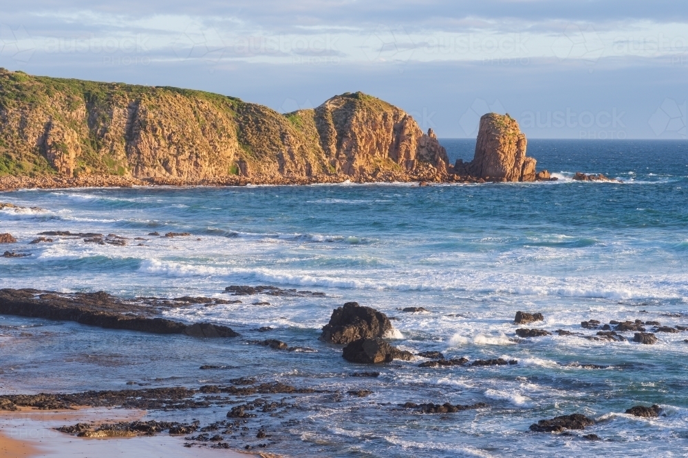 Distant view across a bay to rock formations along a rugged coastline - Australian Stock Image