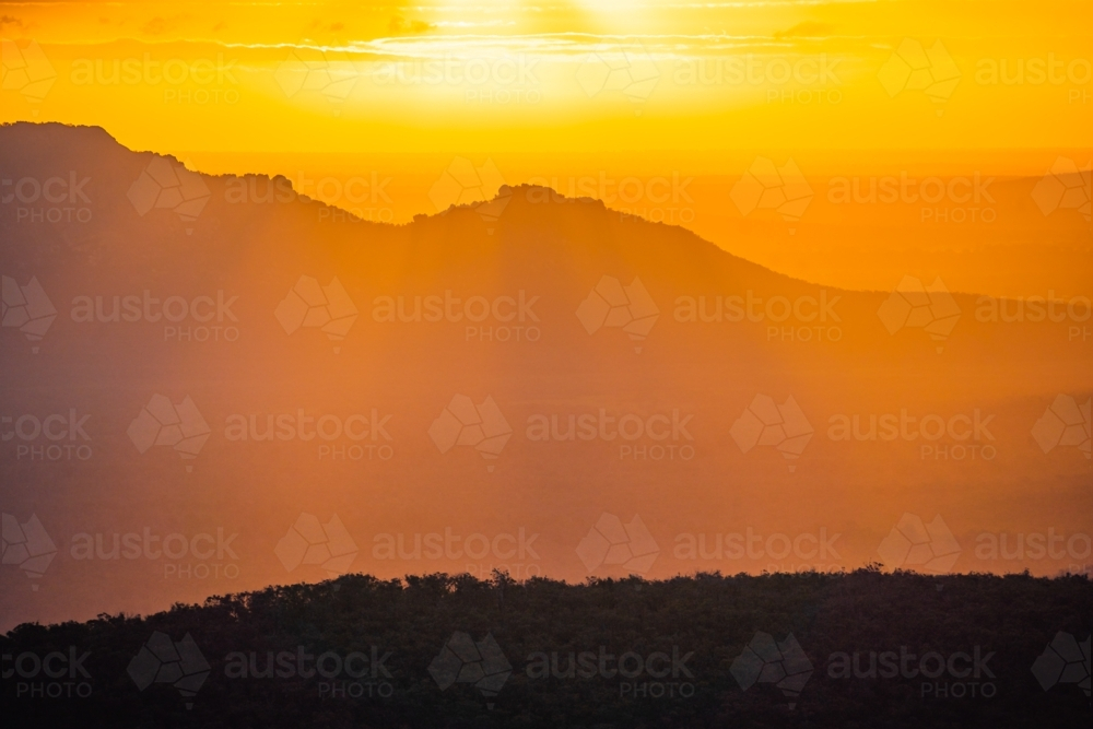 Distant view of a dramatic golden sunset over mountains with rayls of light - Australian Stock Image