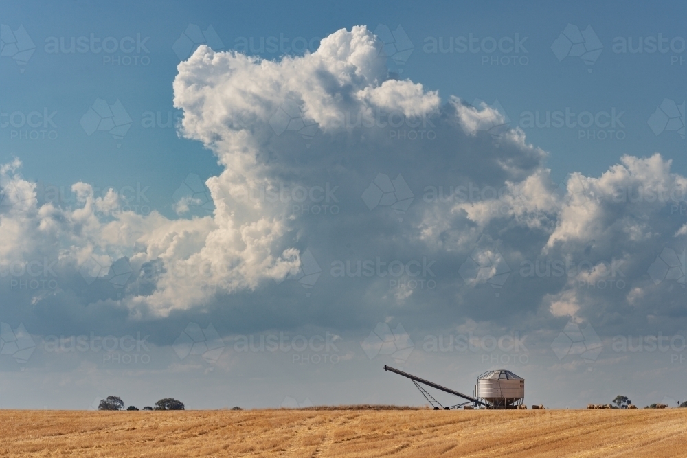 Distant view of a solitary field bin sitting on top of a rise under a dark cloudy sky - Australian Stock Image