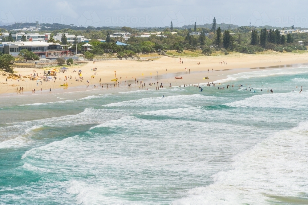 Distant view of beachgoers in the waves along a beach - Australian Stock Image