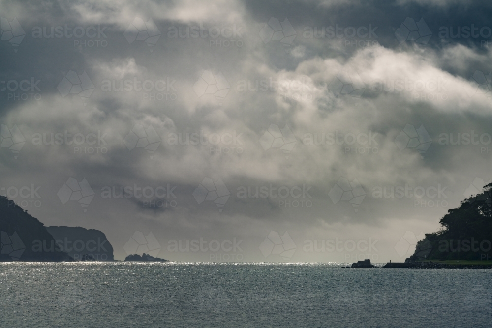 Distant view of dark storm clouds between two coastal headlands in silhouette - Australian Stock Image