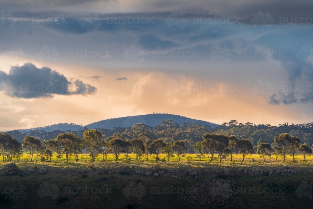 Distant view of dramatic lighting and storm clouds over gum trees and hills - Australian Stock Image