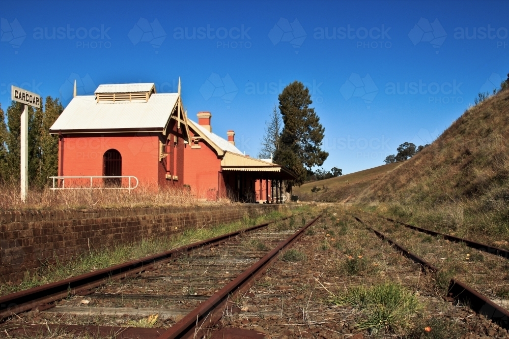 Disused country railway station with blue sky and weeds growing on tracks - Australian Stock Image
