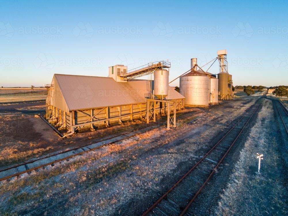 Disused railway tracks running past old grain silos in a rural scene - Australian Stock Image