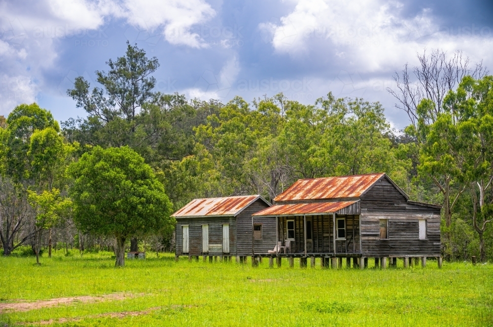 Disused wooden homestead surrounded by grazing field and dramatic stormy sky. - Australian Stock Image