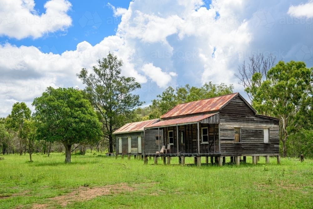 Disused wooden homestead surrounded by grazing field and dramatic stormy sky - Australian Stock Image