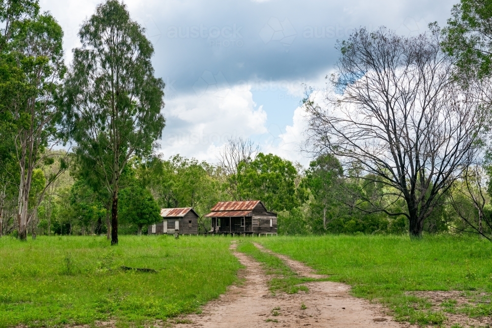 Disused wooden homestead surrounded by grazing field and dramatic stormy sky - Australian Stock Image