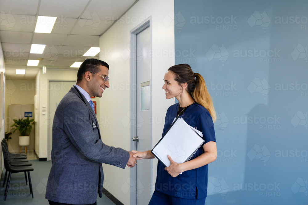 Doctor and nurse shaking hands in office - Australian Stock Image