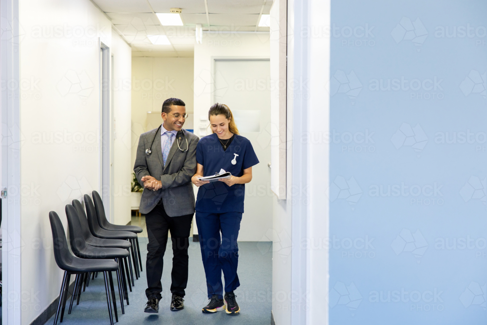 Doctor and nurse talking while walking down office hallway - Australian Stock Image