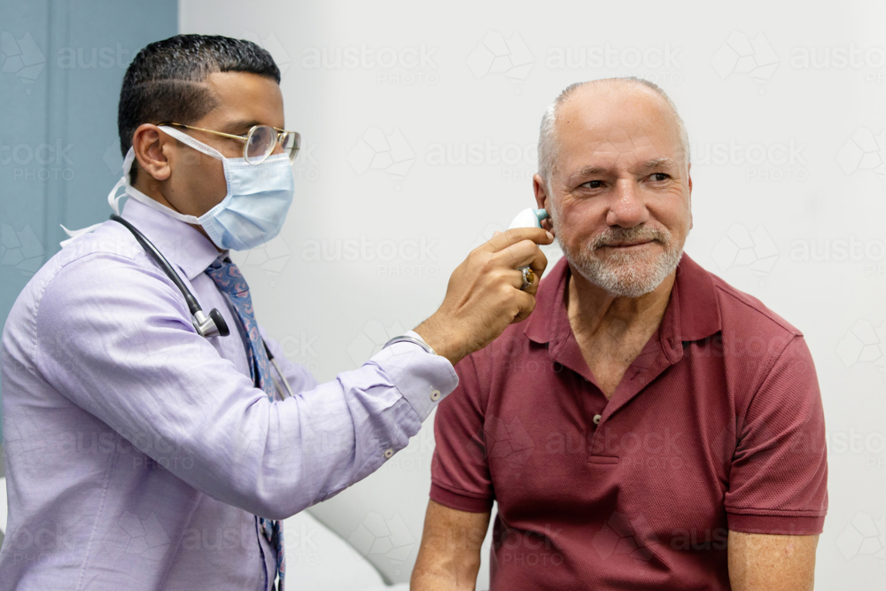 Doctor using ear thermometer on middle-aged patient - Australian Stock Image